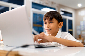 Portrait school boy using digital device in school classroom.