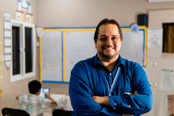 Portrait of latin american male teacher with arms crossed smiling in the class at school - obrazy, fototapety, plakaty
