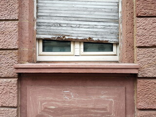 Altbau Fassade aus rotem Gestein mit Fenster, Fensterbank und altem klapprigen Rolladen in Grau mit...
