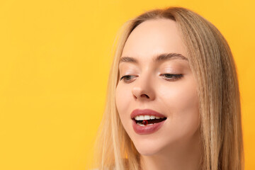 Young woman taking vitamin A pill on yellow background, closeup