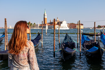 Tourist woman in dress watching gondolas moored by Saint Mark square in city Venice, Veneto,...