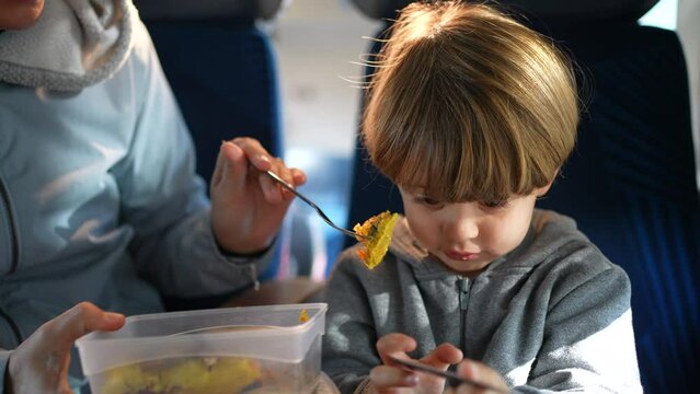 Mother feeding son during train trip. Child passenger being fed food while traveling. Mom holding tupperware and fork