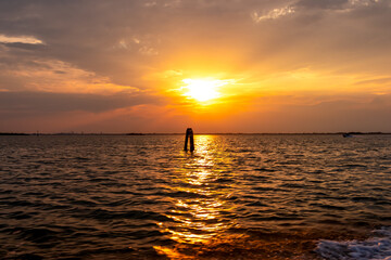 Scenic sunset view over Venetian lagoon seen from a boat in city of Venice, Veneto, Northern Italy, Europe. Reflection in the water creating romantic atmosphere. Orange red sky. Silhoutte of landmarks