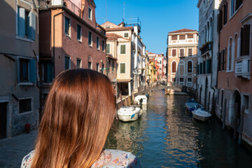 Fototapeta na wymiar Rear view of woman watching water channel in city Venice, Veneto, Italy, Europe. Venetian architectural landmarks and old houses facades along. Urban tourism in summer atmosphere. Romantic vacation