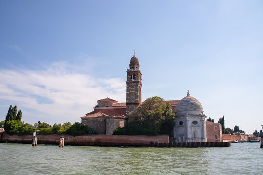 Panoramic view from ferry of Catholic church San Michele in Isola in Venice, Veneto, Italy, Europe. Summer tourism in Venetian lagoon, Adriatic sea. Timber piles indicating waterway. Boat trip