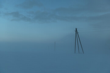 Winter minimalist landscape with electric poles on a foggy snowy field