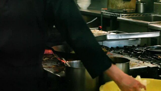 The cook on the kitchen cooks noodels in wok over onover flaming fire very quickly