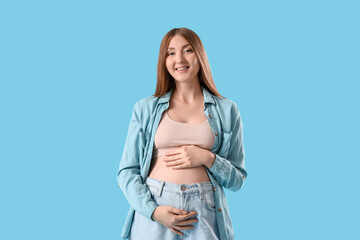Fototapeta premium Young pregnant woman smiling on blue background
