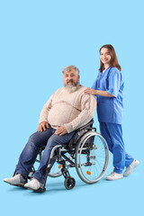 Mature man in wheelchair with nurse on blue background