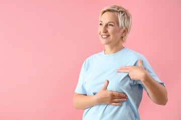 Beautiful mature woman checking her breast on pink background. Cancer awareness concept