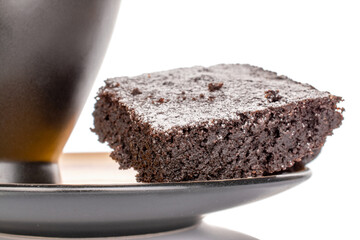 One piece of classic chocolate brownie on ceramic saucer with black cup, macro, isolated on white background.