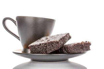Two pieces of classic chocolate brownie on ceramic saucer with black cup, macro, isolated on white background.