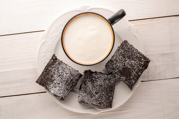 Three pieces of classic chocolate brownie with ceramic saucer and cup with sour cream on wooden...