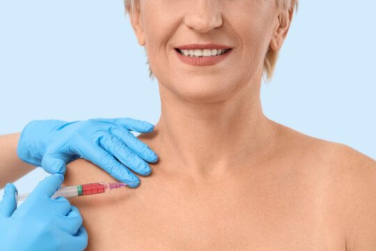 Beautiful mature woman receiving injection on pink background, closeup
