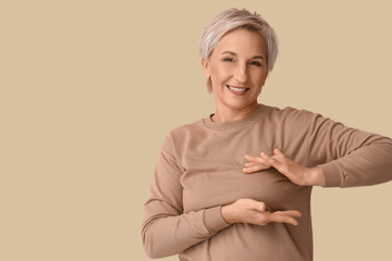 Beautiful mature woman checking her breast on beige background. Cancer awareness concept