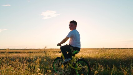 Child boy rides bicycle on grass field. Childs feet are pedaling. Child, cyclist plays, rides, sunset. Pedaling, bicycle wheel. Childrens travel. Physical exercise. Family in park. Kid play lifestyle