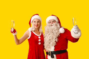 Fototapeta na wymiar Santa and MRS Claus with glasses of champagne on yellow background