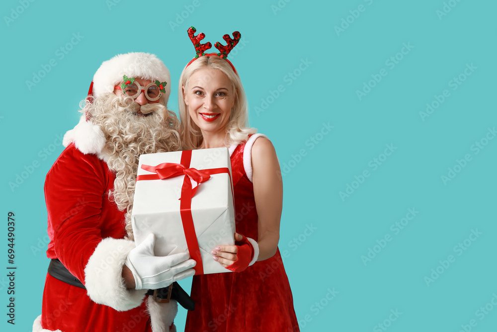 Canvas Prints santa and mrs claus in christmas deer horns with gift box on blue background