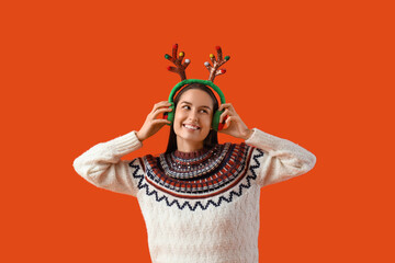 Young woman in reindeer horns on orange background