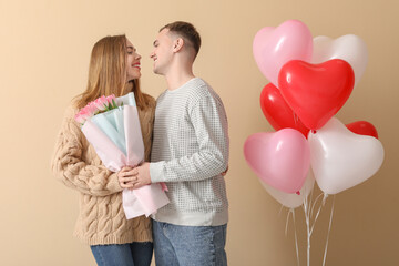 Lovely couple with bouquet of flowers and heart-shaped balloons on beige background. Valentine's...