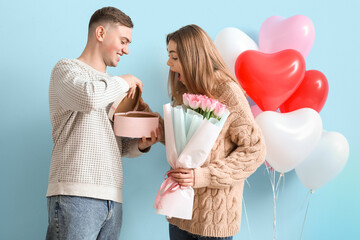 Lovely couple with gift box and heart-shaped balloons on blue background. Valentine's Day...