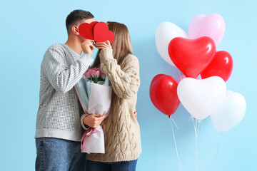 Lovely couple with bouquet of flowers, paper hearts and heart-shaped balloons on blue background....