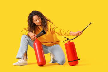 Young African-American woman with fire extinguishers on yellow background