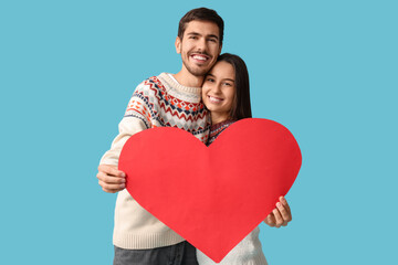 Beautiful young couple with red paper heart on blue background. Valentine's day celebration