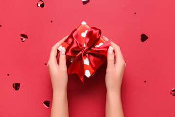 Female hands with gift box and confetti on red background. Valentine's Day celebration