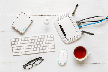 Modern wi-fi router with keyboard and cup of tea on white wooden background