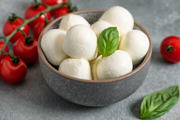Mozzarella cheese balls in a bowl with basil leaves and cherry tomatoes. Side view, selective focus.
