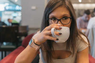 Young woman taking a sip of her delicious coffee. Close up image of a girl tasting her freshly...