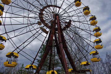 A rusted Ferris wheel with yellow cabins against a cloudy sky.