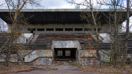 An abandoned structure surrounded by bare, tall trees. An abandoned football stadium in Pripyat. Overgrown with trees ruins of the stadium. © Oleksii