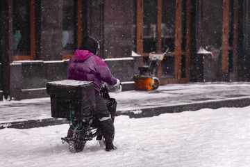 Foto op Canvas A delivery man on an electric motorcycle rides in the snow © Tatiana