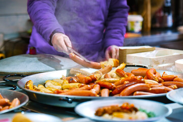 The seller holds a hot sausage in special tongs
