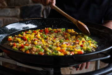 Paella from Spain recipe, fry vegetables in a big paella pan with wood spoon