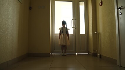 Lonely silhouette of child standing at door, window alone in dark empty hallway. Little girl peeking out window rear view. Primary school, looking into future of child. Difficult childhood loneliness