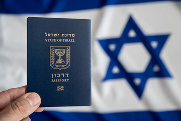 Hand holds an Israeli international passport with the Israeli flag on the background