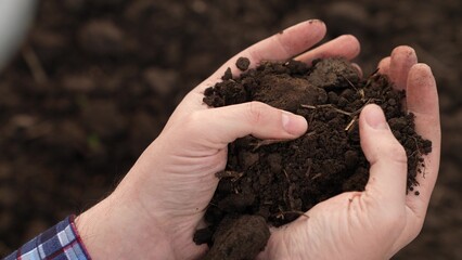 Fertile soil in male hands of farmer. Male hands hold fertile land in field. Organic soil in hands...