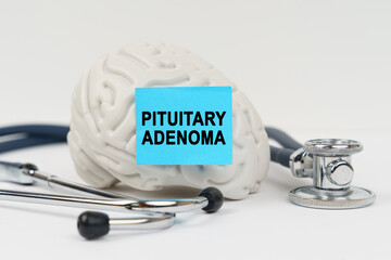 On a white surface next to the stethoscope lies a brain on which a sticker with the inscription - Pituitary adenoma