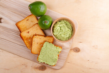 Avocado mash lay on slices of toasted bread atop wooden cutting board placed on wooden table.