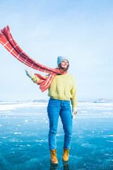 Happy smiling woman traveler in trendy winter hat and scarf looking away while standing outdoors on frozen lake during her trip to Antarctica