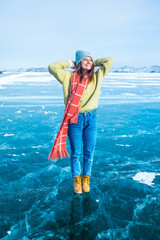 Happy smiling female traveler enjoying good day while standing on frozen Baikal lake with beautiful cracked ice floes inside