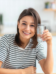 Healthy lifestyle. Happy young woman holding a glass of clean water, looking at the camera and...