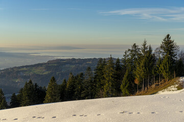 View from snowcovered mountain down onto a lake in evening light