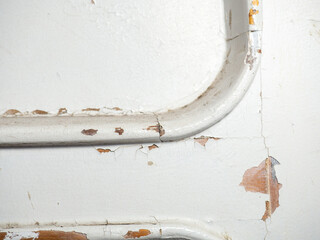 Part of an old door. White paint is coming off the wood. Surface with peeling paint.