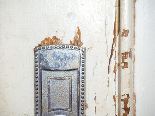 Part of an old door. White paint is coming off the wood. Surface with peeling paint.  Destroyed door handle