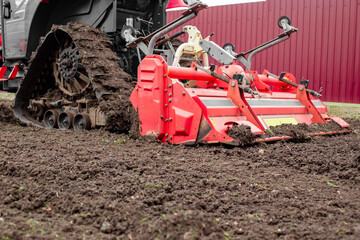 caterpillar tractor with a tillage cutter loosens the soil in a garden plot.