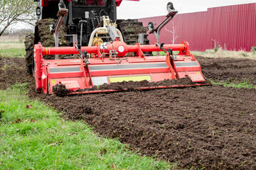 caterpillar tractor with a tillage cutter loosens the soil in a garden plot.